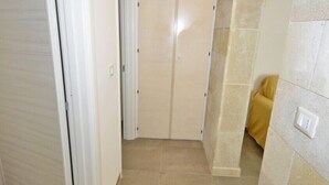 A narrow hallway with beige tiled flooring, white doors, and a stone wall with a light fixture. - Villa Lara (Torre Pali)