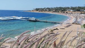 Ein Küstenstrand mit einem Pier, der sich ins Meer erstreckt, ein Sandstrandabschnitt mit Sonnenschirmen und eine Wohngegend im Hintergrund.