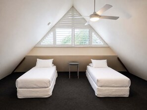 Un dormitorio en áticos pequeño y triangular con dos camas individuales, un ventilador de techo y una mesita.