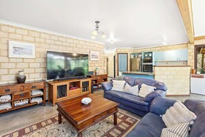 Ein Wohnzimmer mit Fernseher, Holzmöbeln, einem blauen Sofa und einer Küche im Hintergrund.