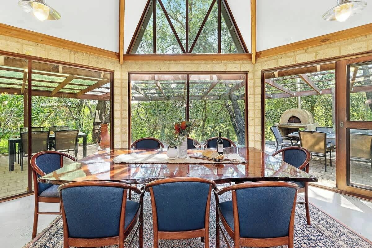A spacious dining area with a large table and chairs, large windows, and a view of the outdoors.