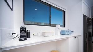 A modern kitchen with a white countertop, a coffee maker, a toaster, and a refrigerator.