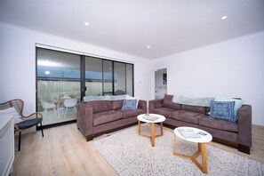 A modern living room with two sofas, a coffee table, and a glass door leading to an outdoor area. - ShoreAcres Retreat—Peaceful Beach Hideaway (Dunsborough)