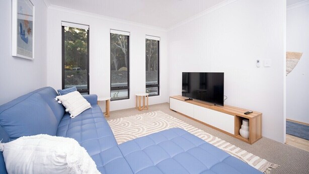 A modern living room with a blue sofa, a flat-screen TV, and large windows.