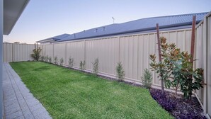 A fenced backyard with a well-maintained lawn and small shrubs.