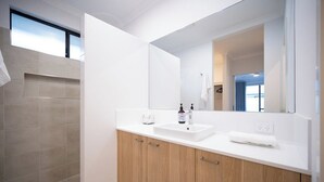 Une salle de bain moderne avec un grand miroir, un lavabo et un espace douche.