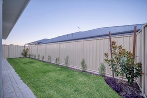 A fenced backyard with a well-maintained lawn and small shrubs.