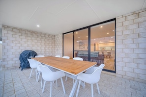A covered patio area with a wooden table and white chairs, a barbecue grill, and a sliding glass door leading to an indoor space. - ShoreAcres Retreat—Peaceful Beach Hideaway (Dunsborough)