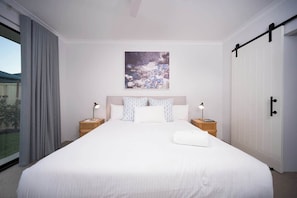 A large bed with white bedding, two bedside tables with lamps, a large window with curtains, and a sliding door.