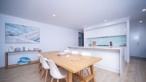 Une cuisine moderne avec des meubles blancs, une table à manger en bois avec des chaises et un tableau accroché au mur.
