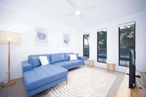 A modern living room with a blue sectional sofa, a standing floor lamp, a patterned rug, and a flat-screen TV. - Shoreacres Retreat - Your next holiday in paradise (Dunsborough)