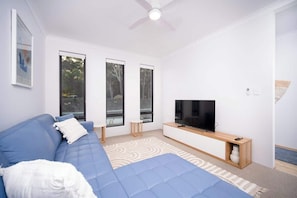 A modern living room with a blue sofa, a flat-screen TV, and large windows.