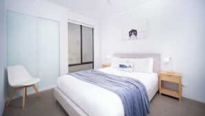 A bedroom with a bed, a chair, a nightstand, a ceiling fan, a window, and a wall-mounted picture.