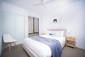 A bedroom with a bed, a chair, a nightstand, a ceiling fan, a window, and a wall-mounted picture. - ShoreAcres Retreat—Peaceful Beach Hideaway (Dunsborough)