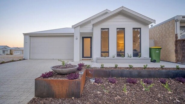 Une maison moderne à deux étages, dotée d’un garage, d’un porche avec un jardinière et d’une poubelle verte.