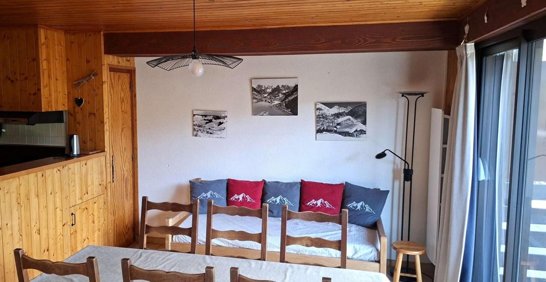 Un interior de madera con una mesa de comedor, sillas, un sofá con cojines con motivos de montaña y una lámpara fijada a la pared.
