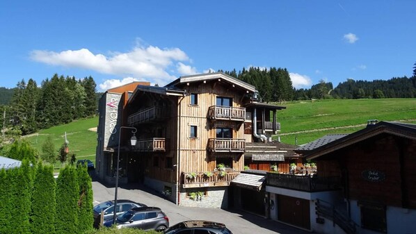 A multi-story wooden building with balconies, a sign reading 'CYCHA', and a view of a green landscape.