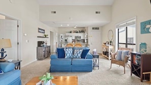 A spacious living room with a blue sofa, a wooden coffee table, and a kitchen in the background. - Feel right at home in this family-sized new listing at the 1MM on the Lake!   (Lake Ozark)