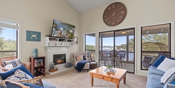 A living room with a fireplace, a large clock, and a view of the outdoors.