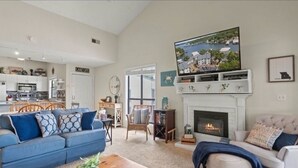 A spacious living area with a fireplace, a television mounted above it, and a kitchen in the background. - Feel right at home in this family-sized new listing at the 1MM on the Lake!   (Lake Ozark)