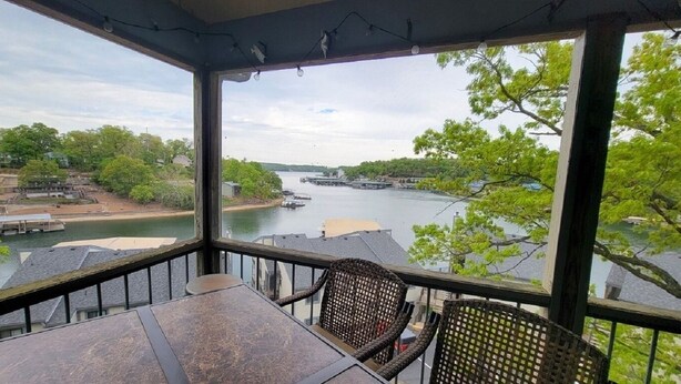 A balcony with a view of a river, a table, and wicker chairs. - Feel right at home in this family-sized new listing at the 1MM on the Lake!   (Lake Ozark)