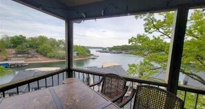 A balcony with a view of a river, a table, and wicker chairs.