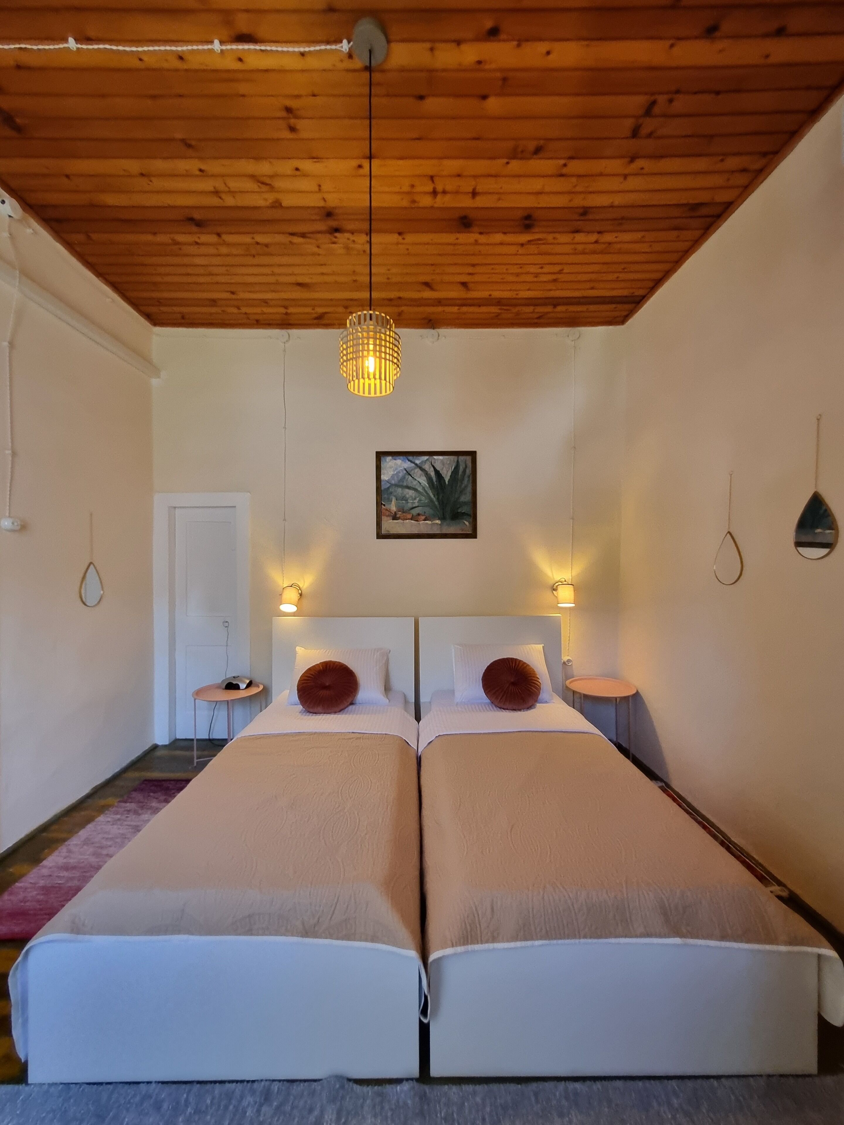 Habitación doble con cama, techo de madera, lámpara colgante, un cuadro en la pared y mesitas de noche con lámparas.