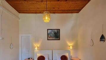 Habitación doble con cama, techo de madera, lámpara colgante, un cuadro en la pared y mesitas de noche con lámparas.