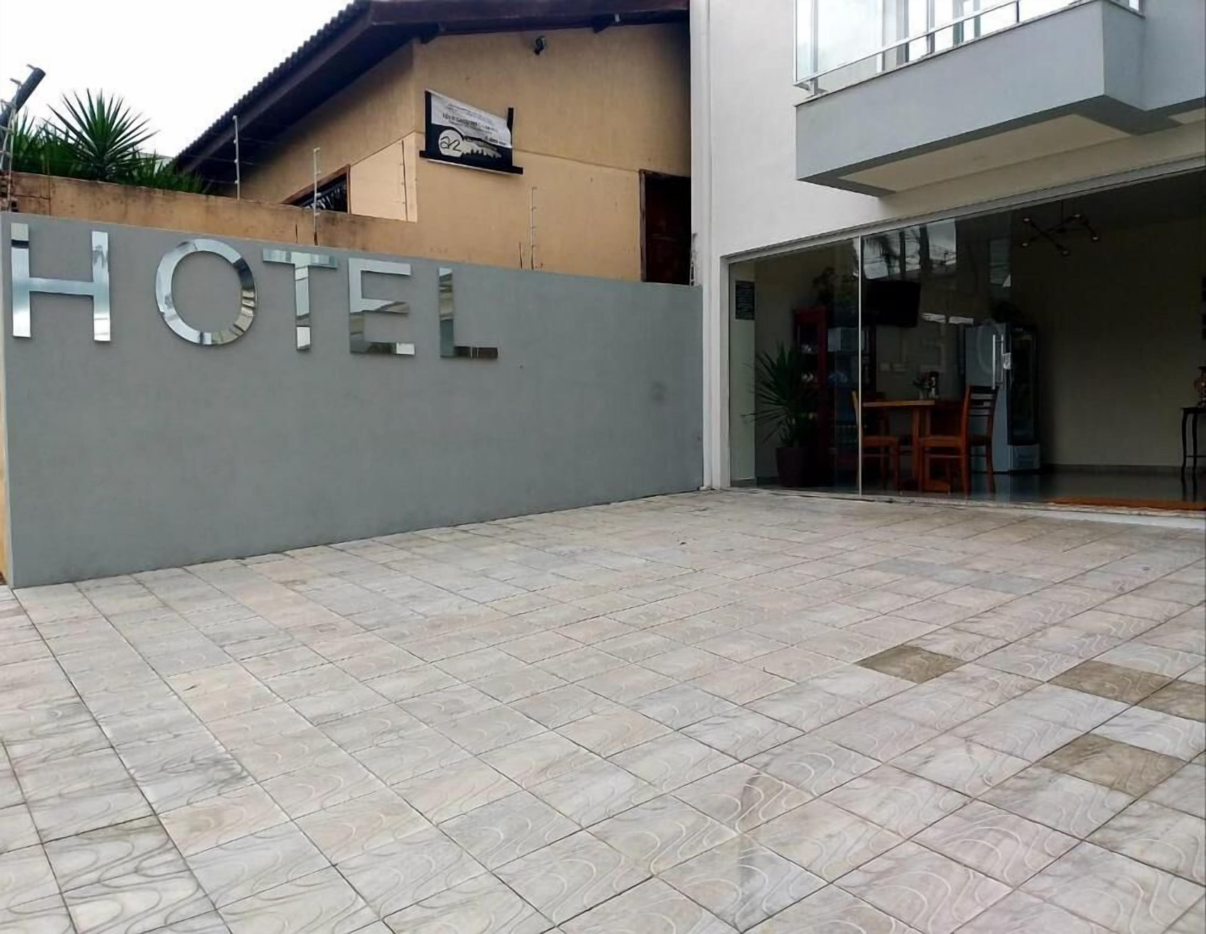 Entrada de un hotel con un letrero grande, un patio con baldosas y una puerta de vidrio que da al interior.