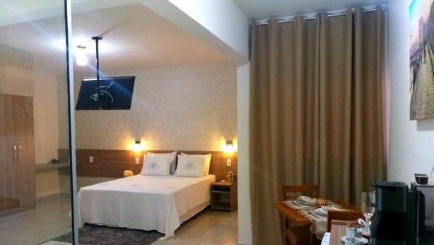 Une chambre d’hôtel comprenant un lit, des tables de chevet, un bureau avec une chaise, une machine à café et un téléviseur fixé au mur.