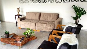 Un salon avec un canapé beige, une table basse en bois agrémentée de plantes, des chaises noires recouvertes de coussins en fausse fourrure blanche et un élément décoratif mural.