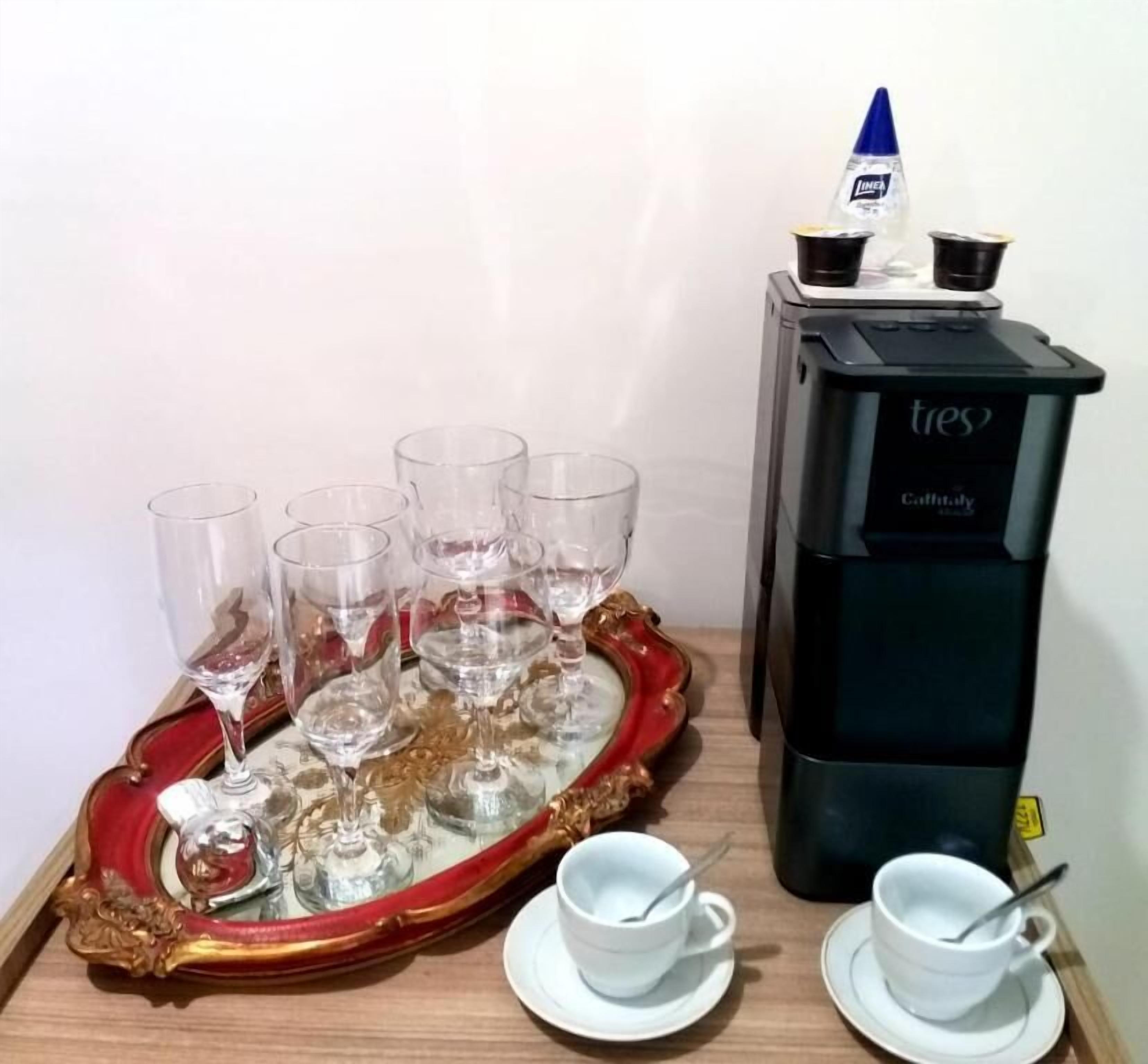 A tray with wine glasses and cups, a coffee machine, and a small blue container.