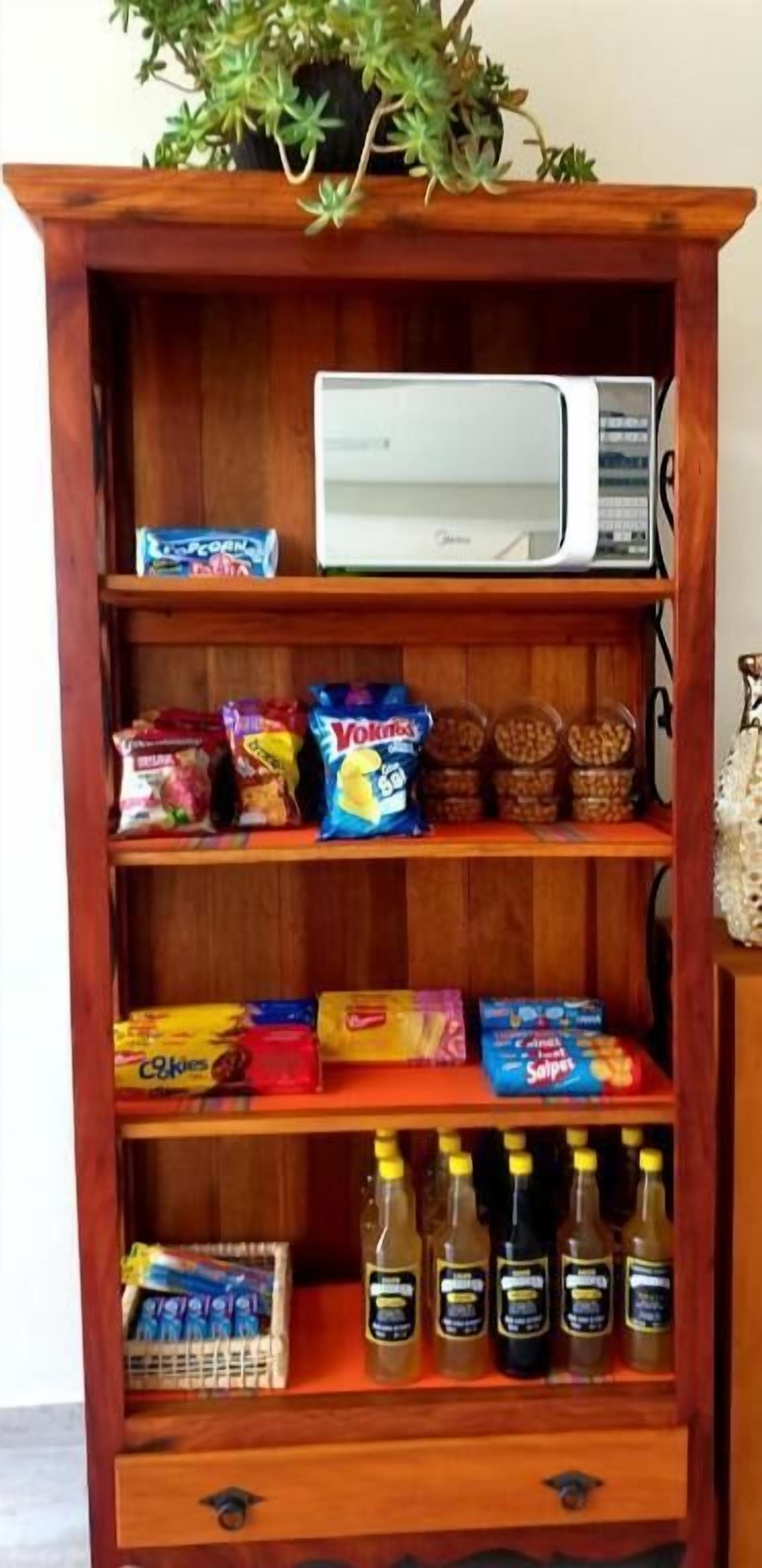 Een houten plank met snacks, een magnetron en flessen.