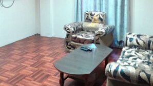 Una sala de estar con un sofá estampado, una mesa de centro y un televisor de pantalla plana montado en la pared.