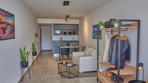 Een modern appartement met een zithoek, kitchenette en een kledingrek met schoenen.