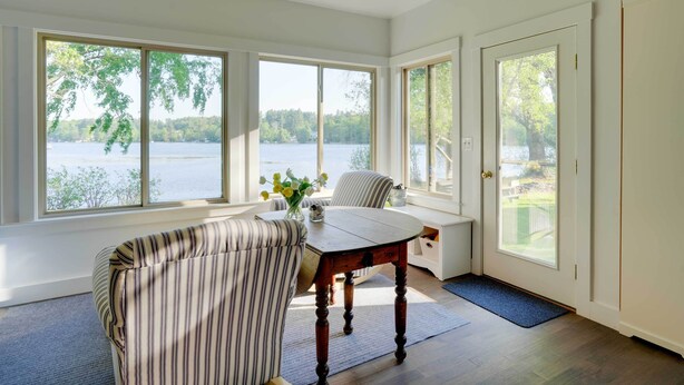 Una habitación con vistas a un lago, una mesa de comedor, dos sillas a rayas y un banco.