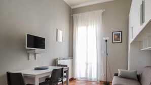Una stanza moderna e luminosa con un tavolo da pranzo, sedie, una TV, un divano e una lampada da terra.