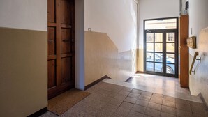 Un corridoio con una porta in legno, una porta di vetro che dà sull'esterno e un telefono fissato al muro.