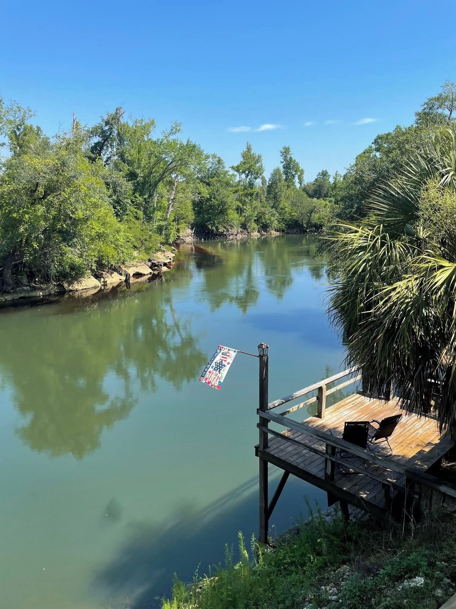 A wooden dock extending into a calm river, surrounded by lush greenery.