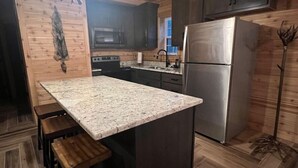 A kitchen with a granite countertop, wooden stools, a stainless steel refrigerator, and dark wooden cabinets. - 4 Bedroom Cabin Retreat (Imperial)