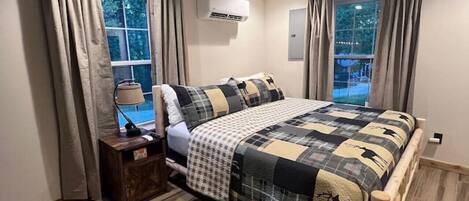 A bedroom with a bed, a ceiling fan, an air conditioning unit, and a window with curtains.