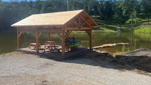 A wooden pavilion with picnic tables by a calm lake, surrounded by trees. - 4 Bedroom Cabin Retreat (Imperial)