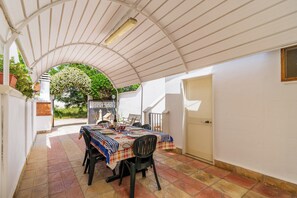 A covered patio with a table set for dining, surrounded by white walls and a tiled floor.