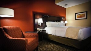 A hotel room with a bed, a chair, a nightstand with a phone, and wall-mounted lamps. - Pearl Street Hotel & Suites (La Crosse)