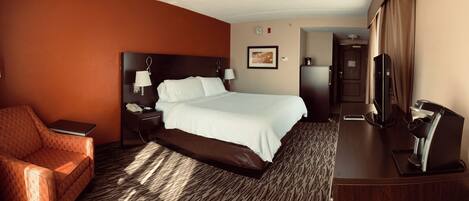 A hotel room with a bed, a desk, a chair, a TV, and a refrigerator.