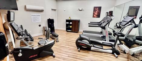 Un gimnasio con máquinas de cardio, máquinas de pesas y un espejo grande.