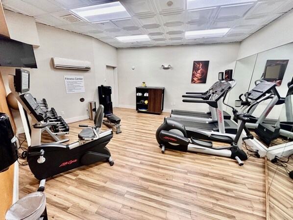 Un gimnasio con máquinas de cardio, máquinas de pesas y un espejo grande.
