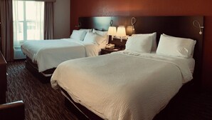 A hotel room with two beds, a bedside table with a lamp, and a window with curtains. - Pearl Street Hotel & Suites (La Crosse)