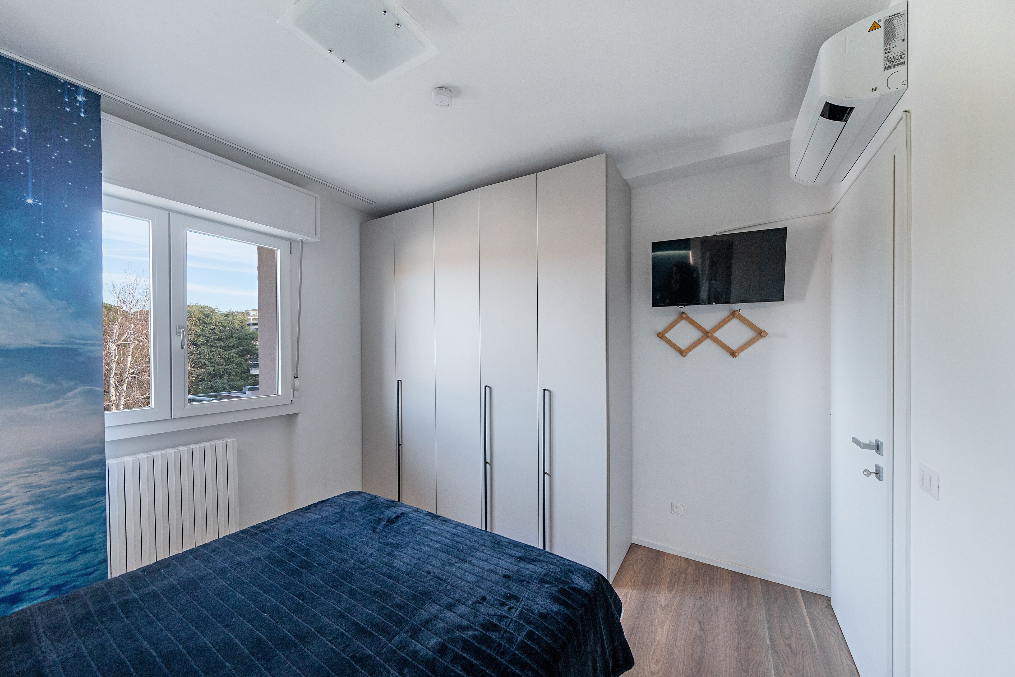 Quarto com cama, guarda-roupa, TV e janela com vista.