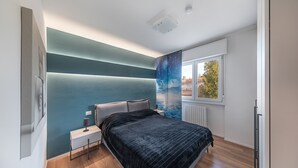 A modern bedroom with a bed, nightstand, and a view of the outdoors through a window. - Maisonnette Il Todeschino B12 by Wonderful Italy (Sirmione)